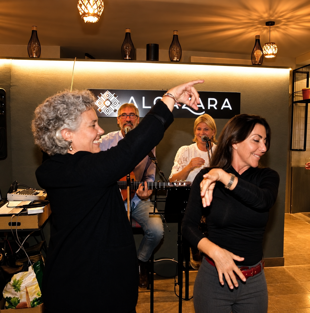 Dos mujeres bailando, con las caras completas y los músicos al fondo, durante una actuación en Algazara